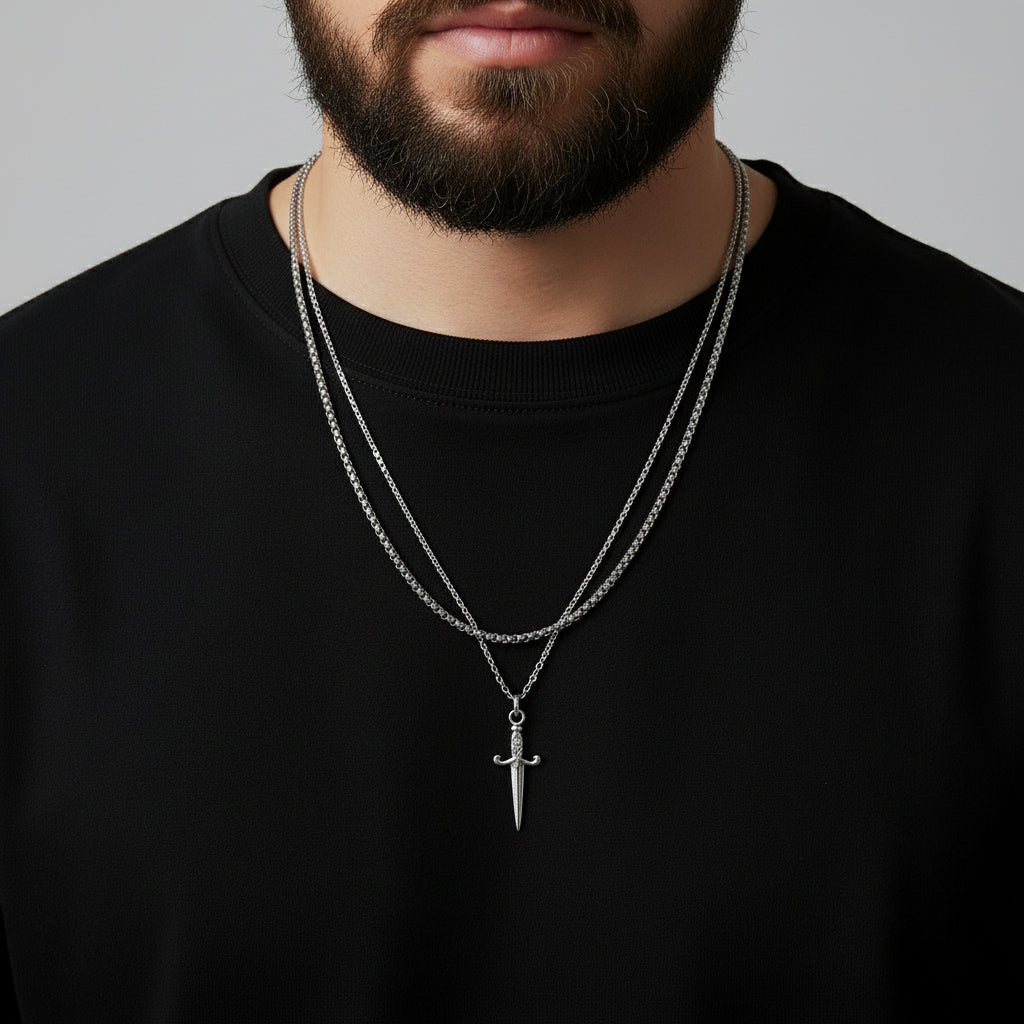 Man wearing a black shirt with a silver chain necklace featuring a sword pendant.